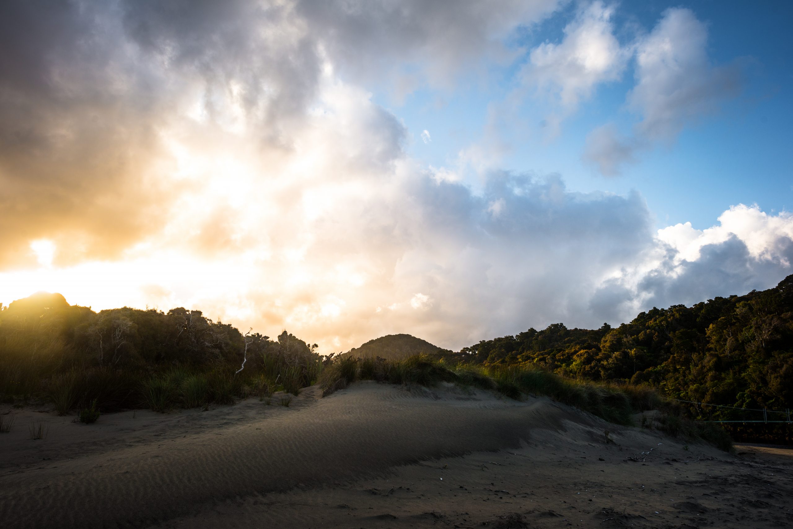 Looking up a sandy hill in New Zealand towards a cloud filled glowing sky